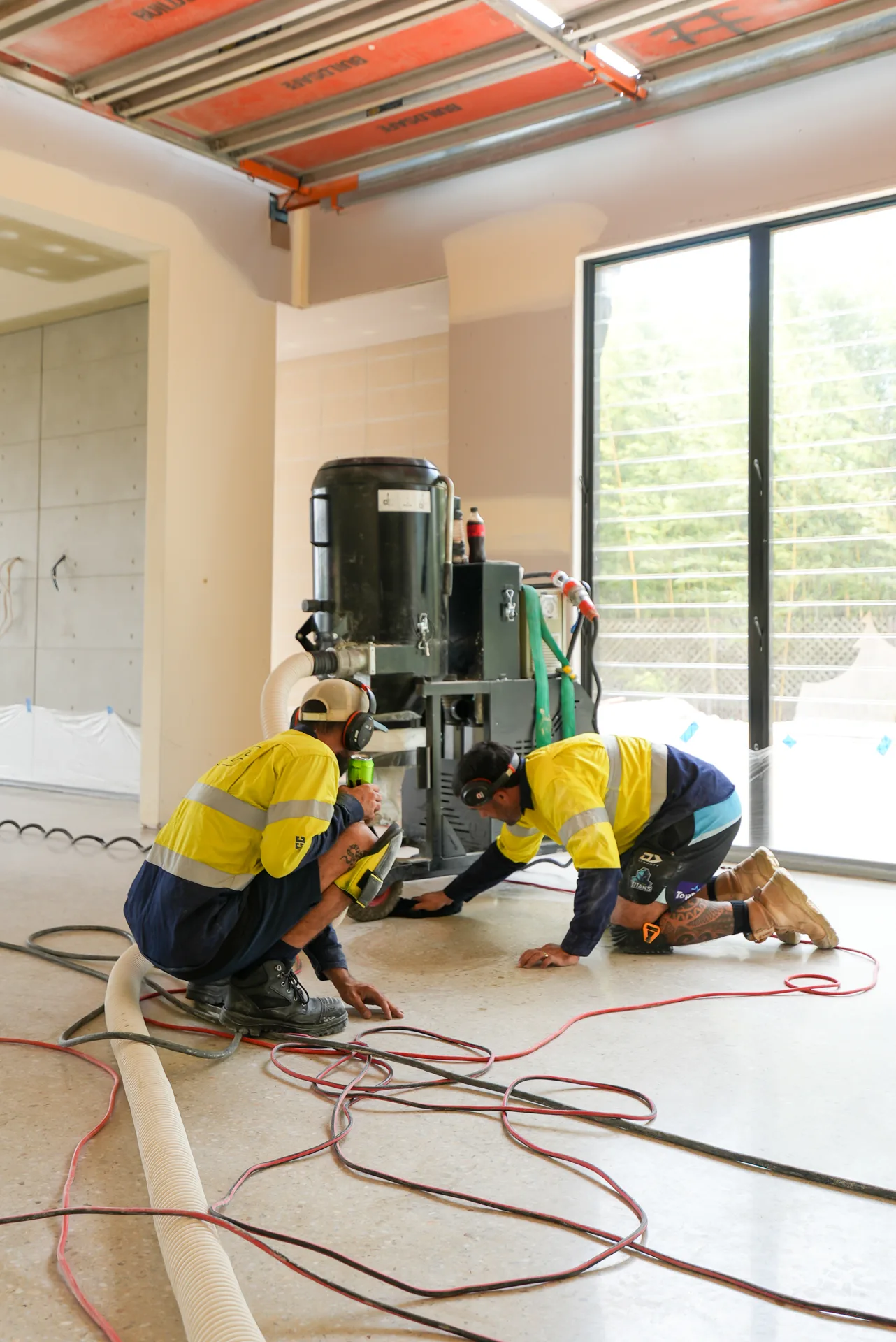 Two ICGC crew members with Husqvarna dust extraction unit polishing concrete in a Brisbane commercial space
