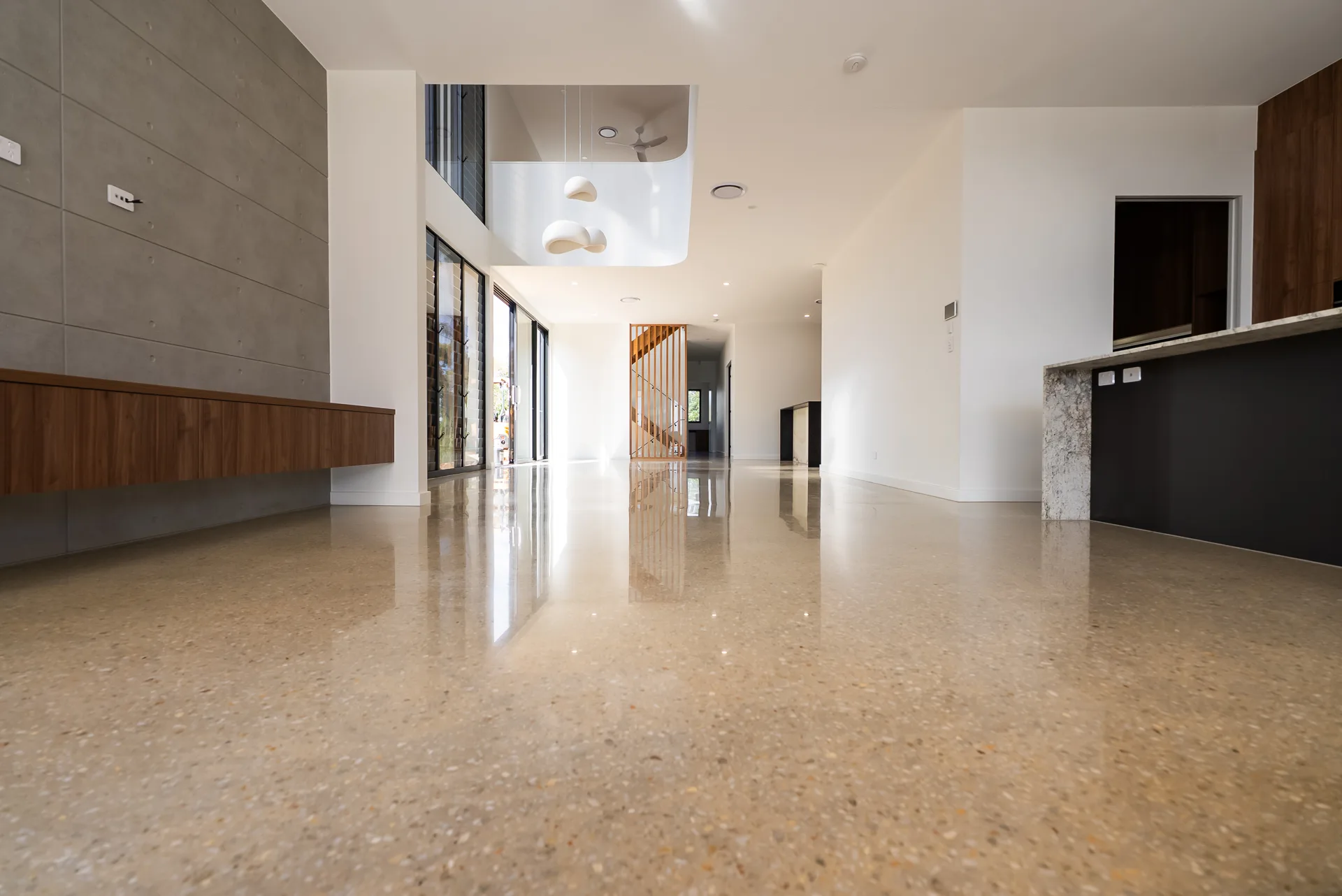 Wide open-plan living area with warm gold-aggregate polished concrete floor and double-height void at a Holland Park home in Brisbane