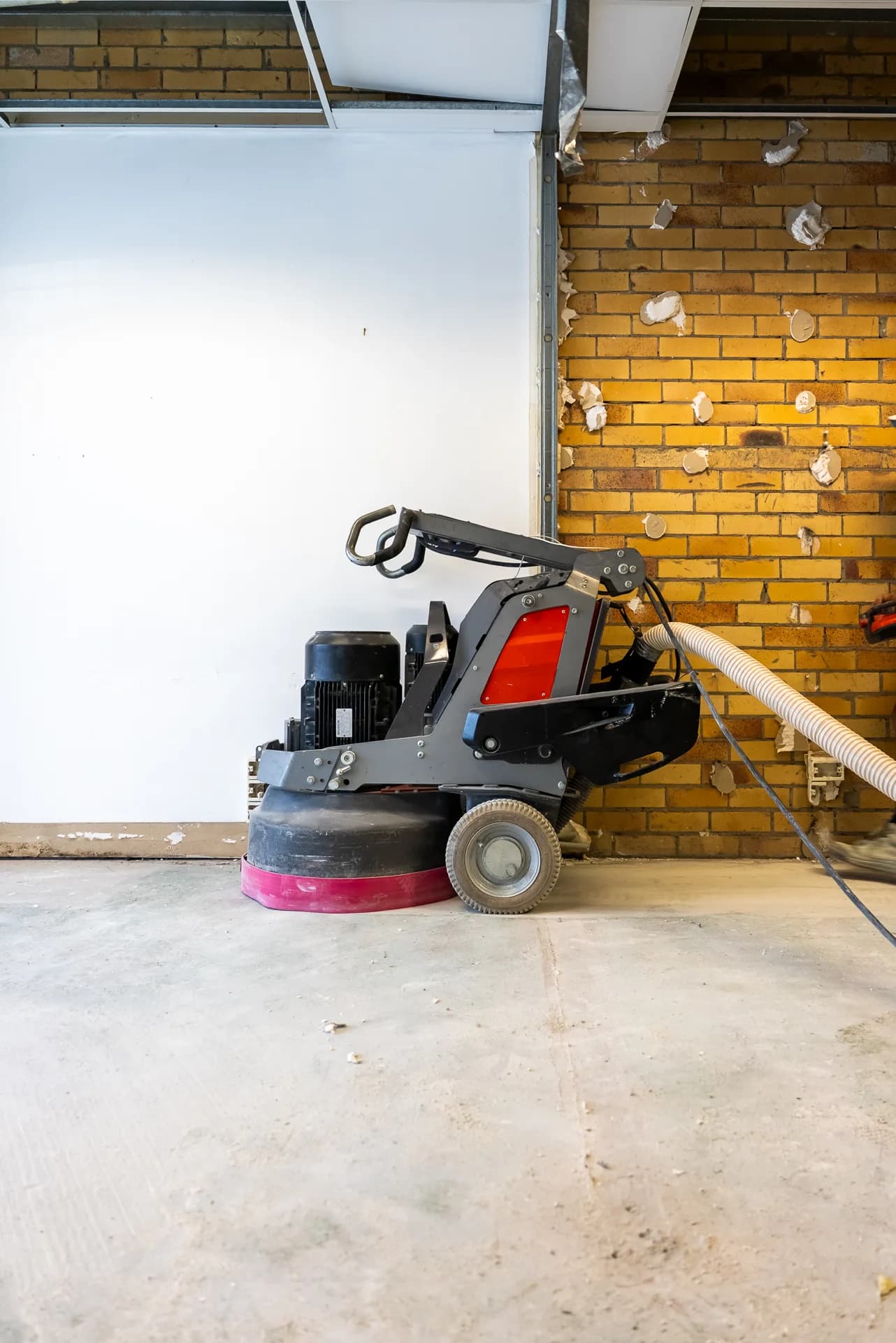 Husqvarna planetary grinder with dust extraction hose in a commercial fitout with exposed brick walls