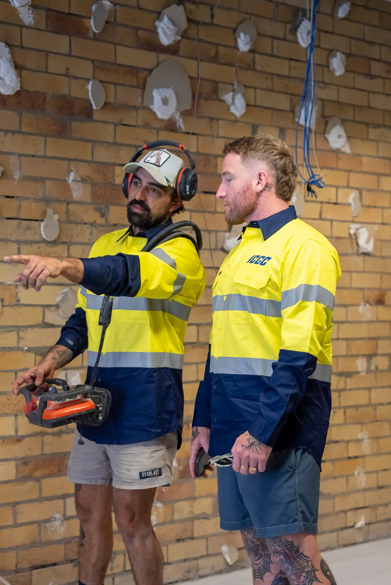 Two ICGC team members in branded hi-vis discussing the grinding plan with equipment on a commercial site